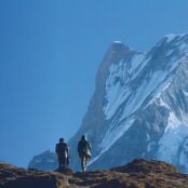 Two people walking on a mountain in Hindu Kush Himalaya. View with a peak behind and a blue sky.