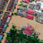 An aerial viewpoint of houses surrounded by brown floodwater.
